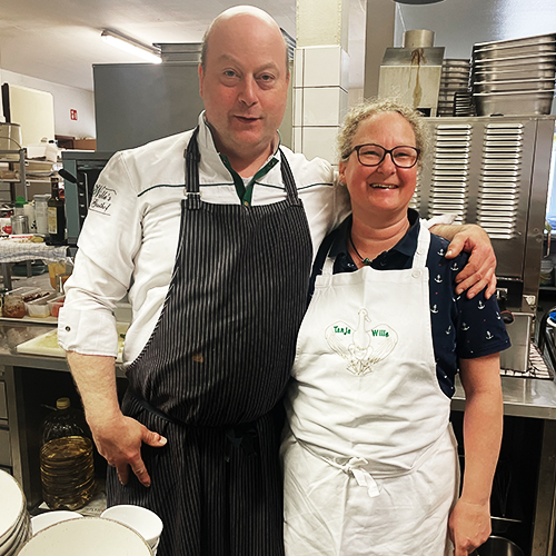 Ein Koch und eine Köchin stehen mit Schürzen in einer Küche