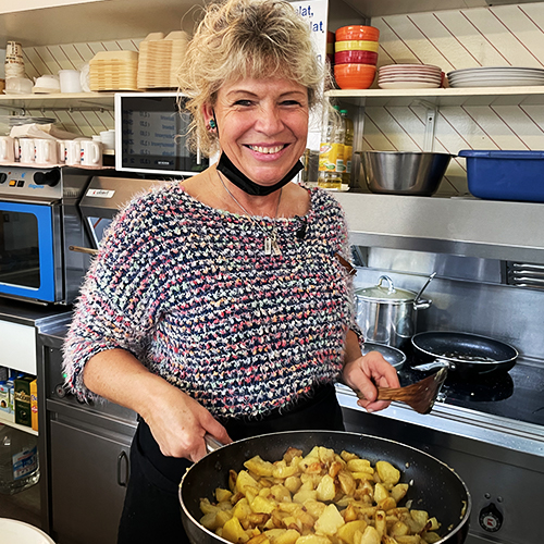 Frau steht mit einer Pfanne voll Bratkartoffeln in einer Küche