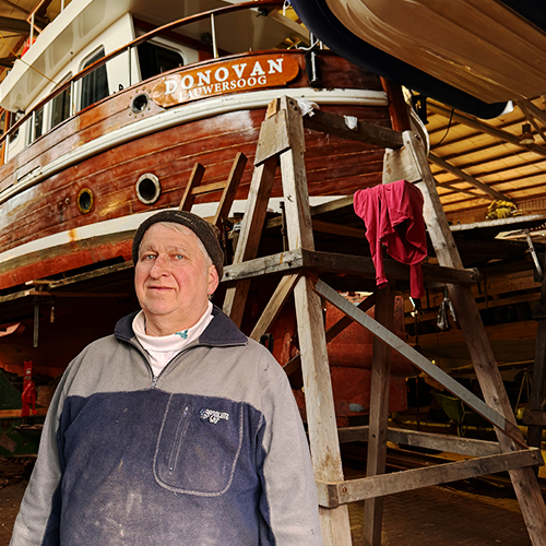 Bootsbauer steht vor Holzboot in Bootswerft