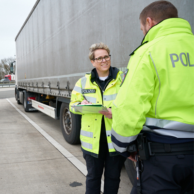 Zwei Polizisten stehen vor LKW zur Kontrolle